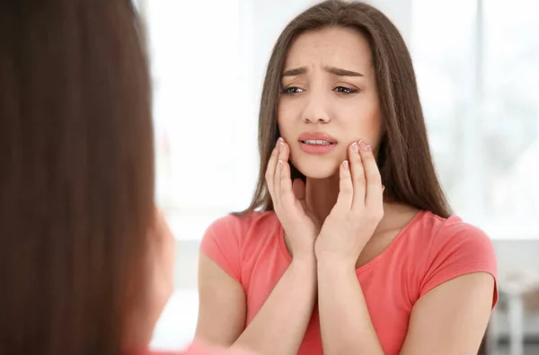 Reflection of woman with sensitive teeth in mirror indoors — Stock Photo, Image