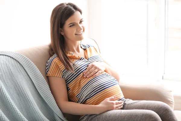 Jovem grávida sentada no sofá na sala de estar — Fotografia de Stock