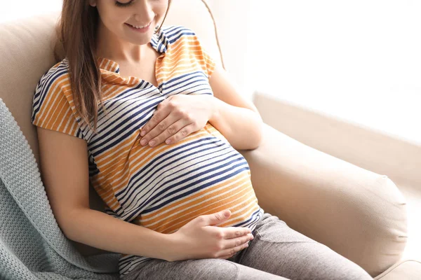Молодая беременная женщина сидит на диване в гостиной — стоковое фото