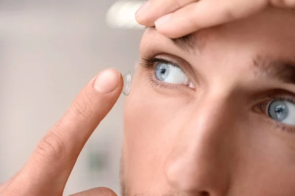 Joven poniendo lente de contacto en su ojo sobre fondo de luz — Foto de Stock