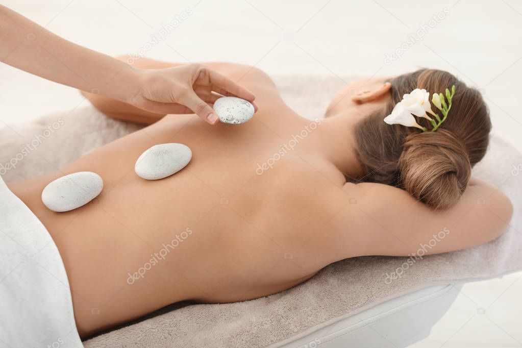 Young woman having traditional hot stones massage in spa salon