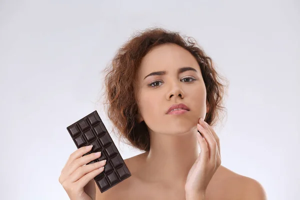 Hermosa mujer joven con problemas de acné celebración de chocolate sobre fondo claro. Alergia cutánea — Foto de Stock