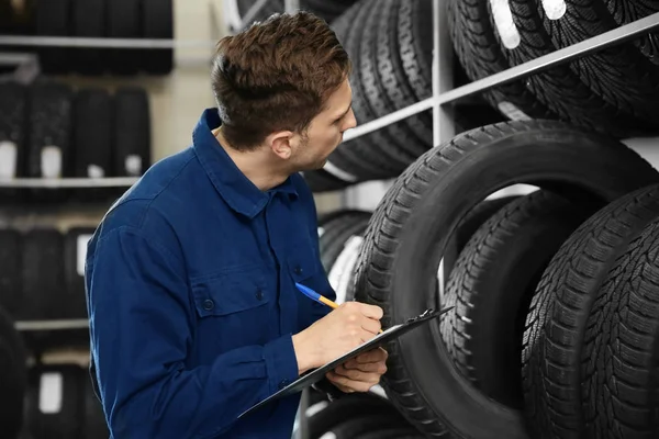 Jovem mecânico masculino com prancheta perto de pneus no centro de serviços de automóveis — Fotografia de Stock