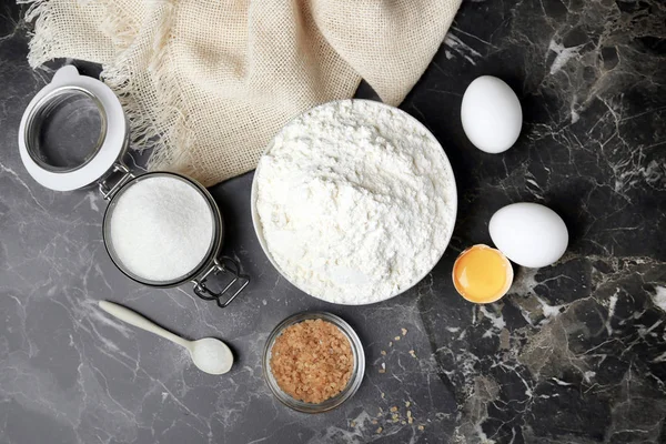 Cuenco con harina, huevos y azúcar sobre fondo gris, vista superior — Foto de Stock