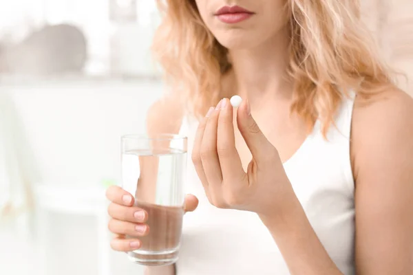 Mujer joven con píldora y vaso de agua en el interior — Foto de Stock