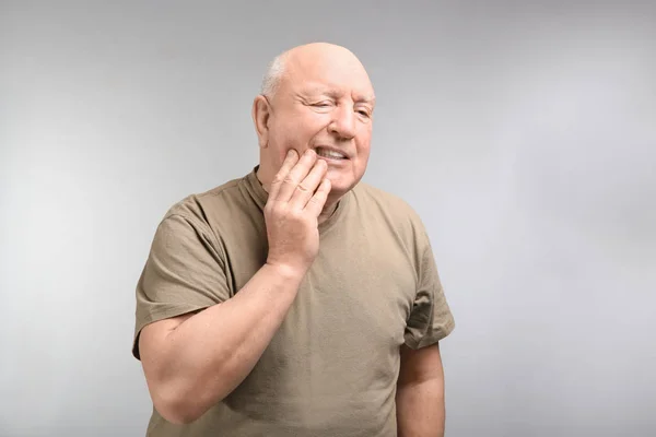 Seniorchef leidet an Zahnschmerzen vor hellem Hintergrund. Dauerhafte Schmerzen — Stockfoto