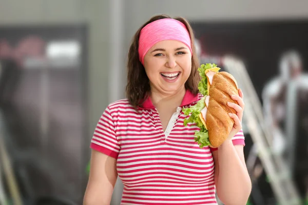 Overweight woman eating sandwich in gym