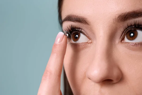 Jovem mulher colocando lente de contato em seu olho no fundo de cor — Fotografia de Stock