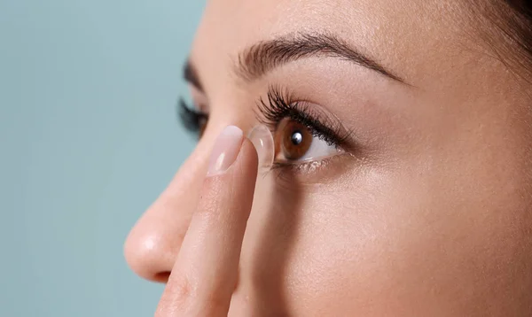 Jovem mulher colocando lente de contato em seu olho no fundo de cor — Fotografia de Stock
