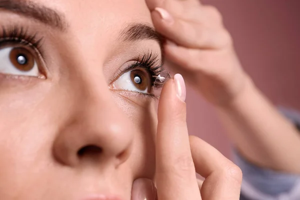 Mujer joven poniendo lente de contacto en su ojo sobre el fondo de color — Foto de Stock