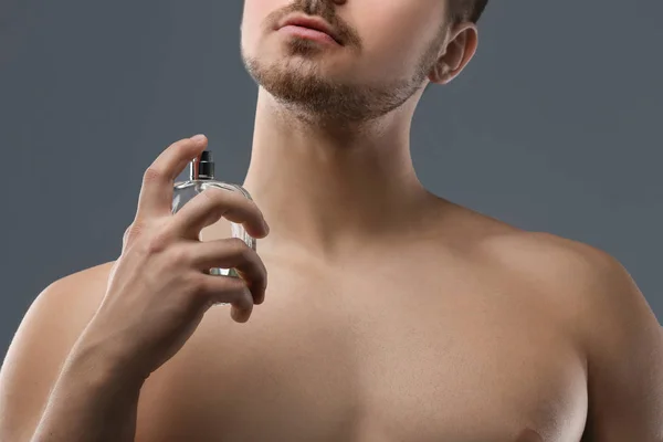 Bonito homem usando perfume no fundo cinza, close-up — Fotografia de Stock