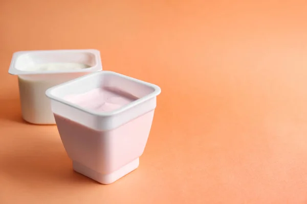 Bicchieri di plastica con gustoso yogurt su sfondo colore — Foto Stock