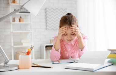 Küçük kız masada kapalı ev ödevi yaparken baş ağrısı acı