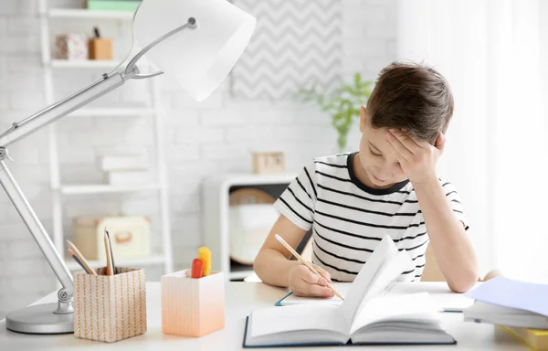 Anak kecil yang menderita sakit kepala saat mengerjakan PR di dalam meja — Stok Foto