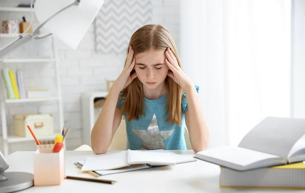 Adolescente que sofre de dor de cabeça ao fazer lição de casa na mesa dentro de casa — Fotografia de Stock
