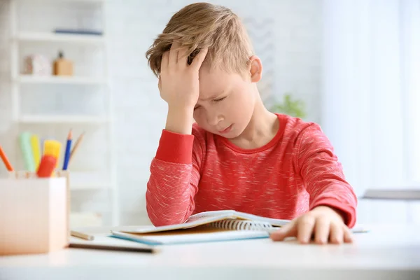 Kleiner Junge leidet unter Kopfschmerzen bei Hausaufgaben am Tisch im Haus — Stockfoto