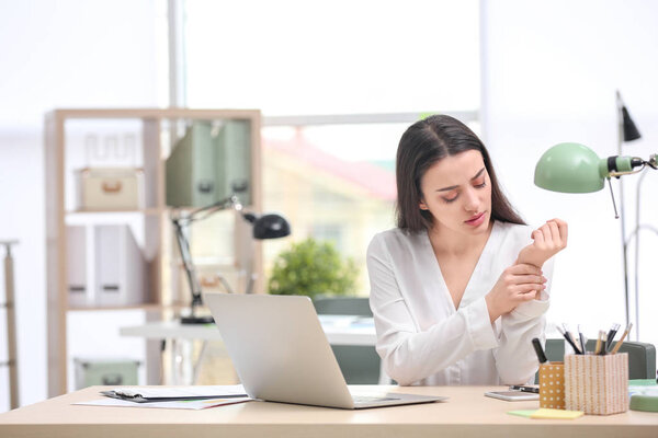 Young woman suffering from wrist pain in office