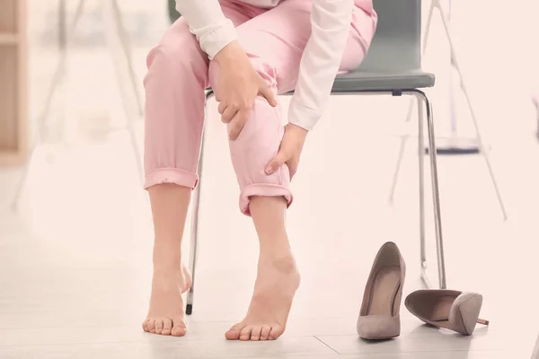 Jeune femme souffrant de douleurs aux jambes au bureau — Photo