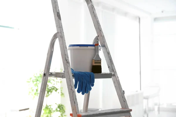 Cubo con pintura, pincel y guantes en escalera en la sala de luz — Foto de Stock