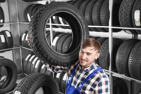 Jovem mecânico masculino com pneu de carro no centro de serviços de automóveis — Fotografia de Stock