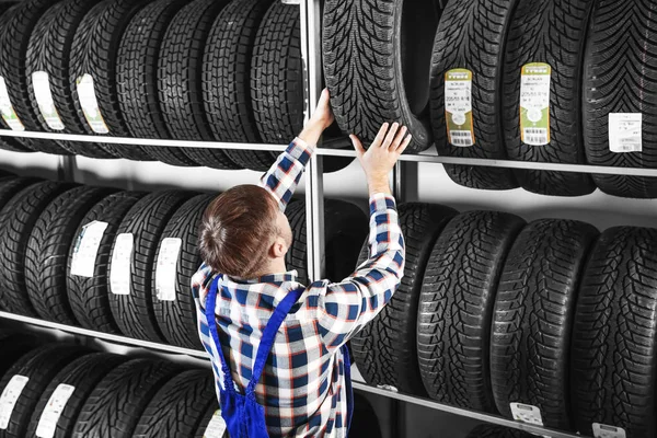 Jovem mecânico masculino com pneus de carro no centro de serviços de automóveis — Fotografia de Stock