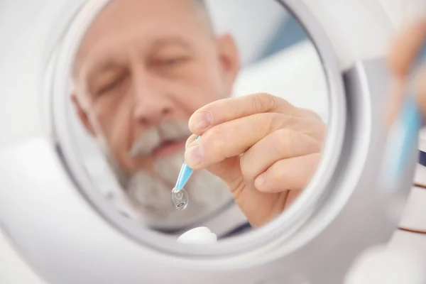 Зеркальное отражение пожилого человека, вынимающего контактные линзы из контейнера — стоковое фото