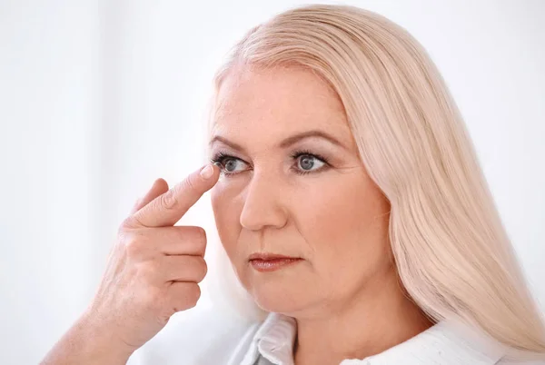 Senior kobieta umieszczenie soczewki w oku na jasnym tle — Zdjęcie stockowe