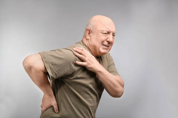 Starší muž trpí bolestí v rameni na světlé pozadí — Stock fotografie