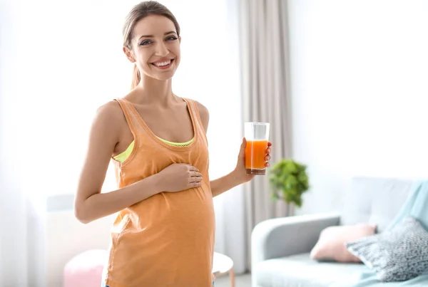 Jovem grávida segurando vidro com suco em casa — Fotografia de Stock