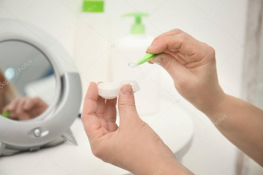 Senior woman taking contact lens from container in front of mirror