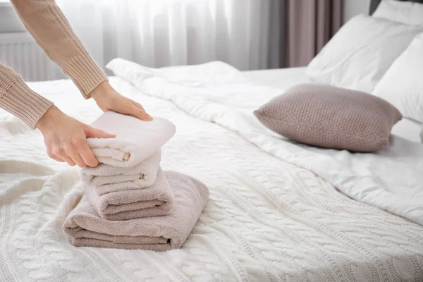 Woman folding clean towels on bed, closeup