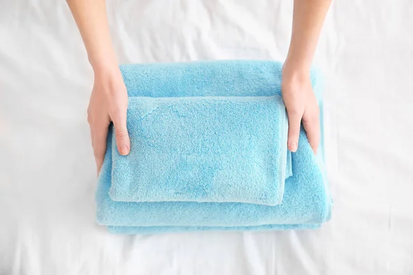 Woman folding clean towels on bed, closeup