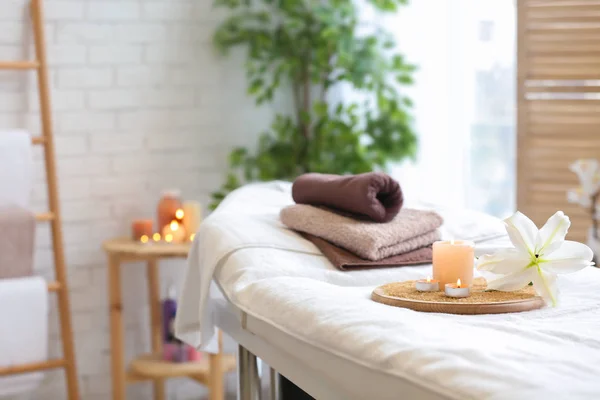 Handdukar, ljus och blomma på massagebänk i spasalong — Stockfoto