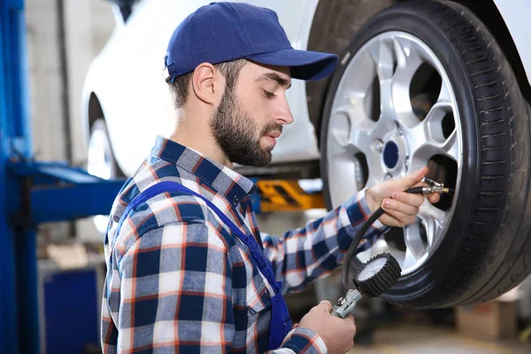 Jovem mecânico verificar a pressão do pneu no centro de serviço — Fotografia de Stock