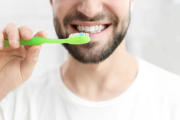 Young man brushing his teeth indoors — Stock Photo, Image