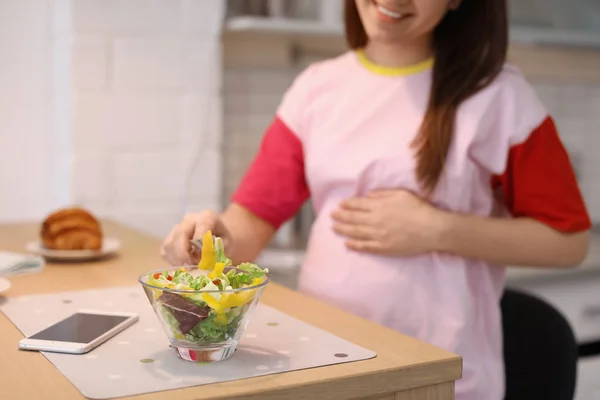 Jeune femme enceinte mangeant de la salade de légumes à table dans la cuisine — Photo