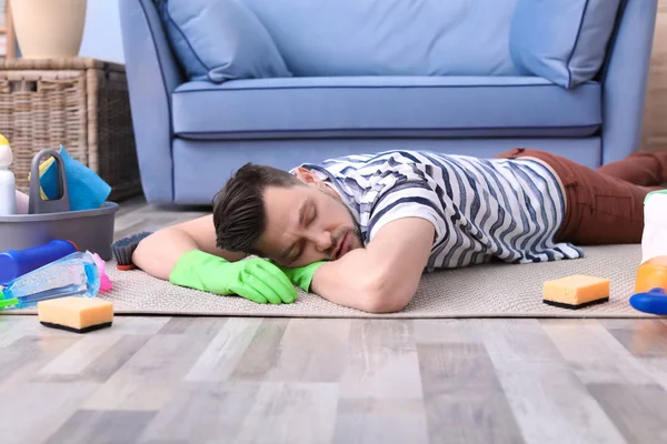 Уставший мужчина спит на полу после уборки ковра дома — стоковое фото