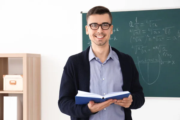 Giovane insegnante maschio con libro in piedi in aula — Foto Stock