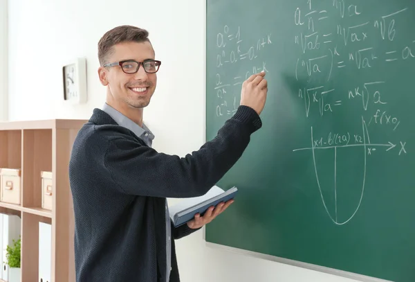 Ung manlig lärare skriver på tavlan i klassrummet — Stockfoto