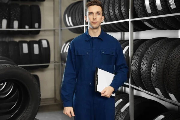 Young male mechanic with clipboard near tires in automobile service center