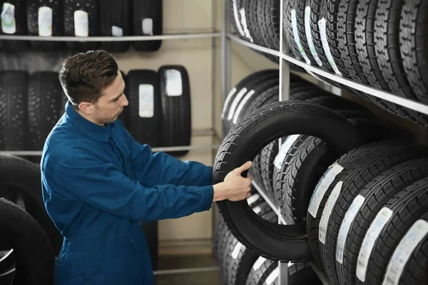 Joven mecánico masculino con neumáticos de coche en el centro de servicio de automóviles —  Fotos de Stock