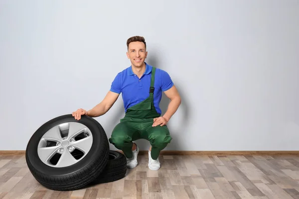 Mecânico masculino com pneus de carro no fundo da parede leve — Fotografia de Stock