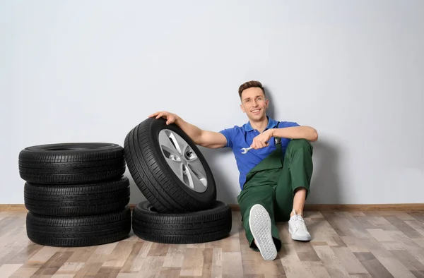 Mecânico masculino com pneus de carro no fundo da parede leve — Fotografia de Stock