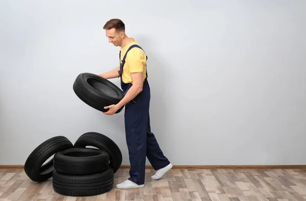 Male mechanic with car tires on light wall background — Stock Photo, Image