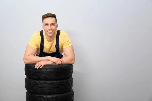 Mecânico masculino com pneus de carro no fundo claro — Fotografia de Stock