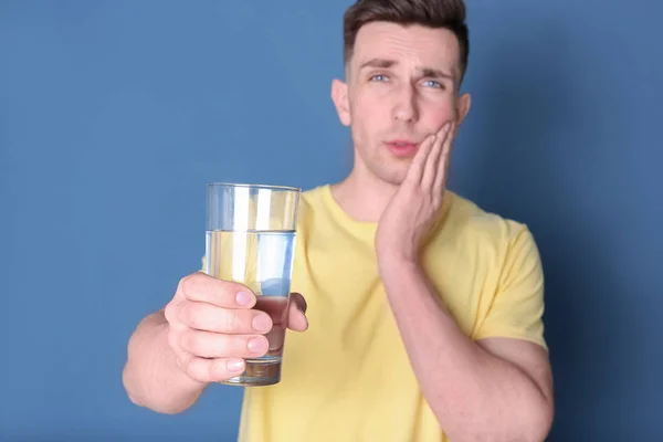 Jeune homme avec des dents sensibles et verre d'eau froide sur fond de couleur — Photo