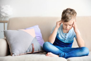 Küçük çocuk evde kanepede otururken baş ağrısı acı