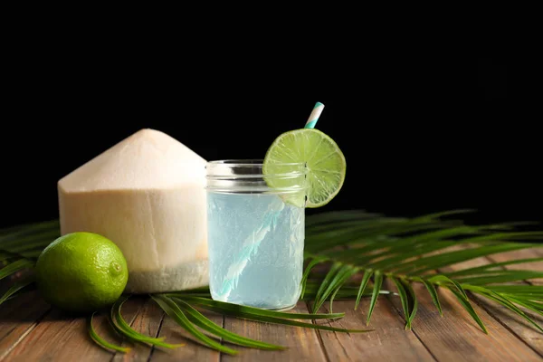 Tarro con agua de coco fresca y lima sobre la mesa sobre fondo negro — Foto de Stock