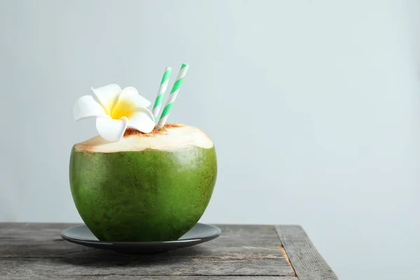 Cocco verde fresco con cannucce da bere e fiore sul tavolo sullo sfondo chiaro — Foto Stock