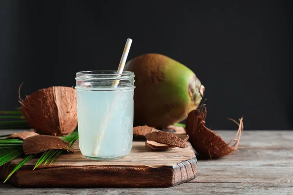 Hermosa composición con frasco de vidrio de agua de coco en la mesa sobre fondo oscuro — Foto de Stock